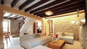 A spacious living area with a stone wall, a wooden staircase, and a white sofa set. - Villa Alordes, Newly renovated house with mountain views (Pollença)