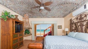 A bedroom with a brick ceiling, a bed with a patterned bedspread, a wooden dresser, a bench, and a view of the beach through a door. - Casa San Miguel Beachfront House (Puerto Peñasco)