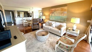 A living room with a sofa, armchairs, a coffee table, and a TV. There is a kitchen in the background. - Vanderbilt Beach Access and on the intercostal! (Naples)