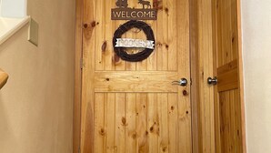 Une porte en bois avec une pancarte « BIENVENUE » et une banderole représentant des « GRENOUILLES », un paillasson et un hall d’entrée recouvert d’une moquette.