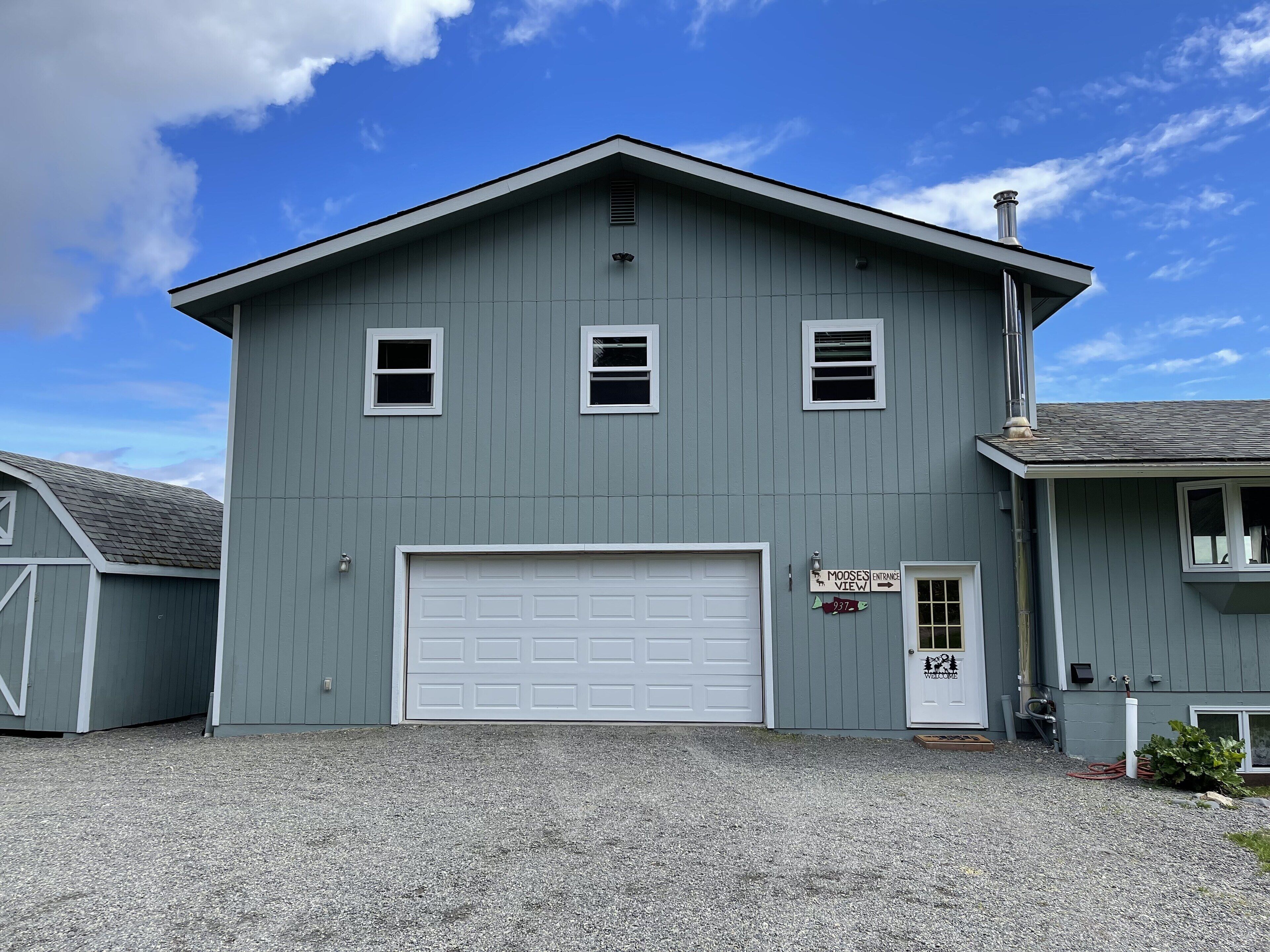A two-story building with a white garage door, a small porch, and a gravel driveway.