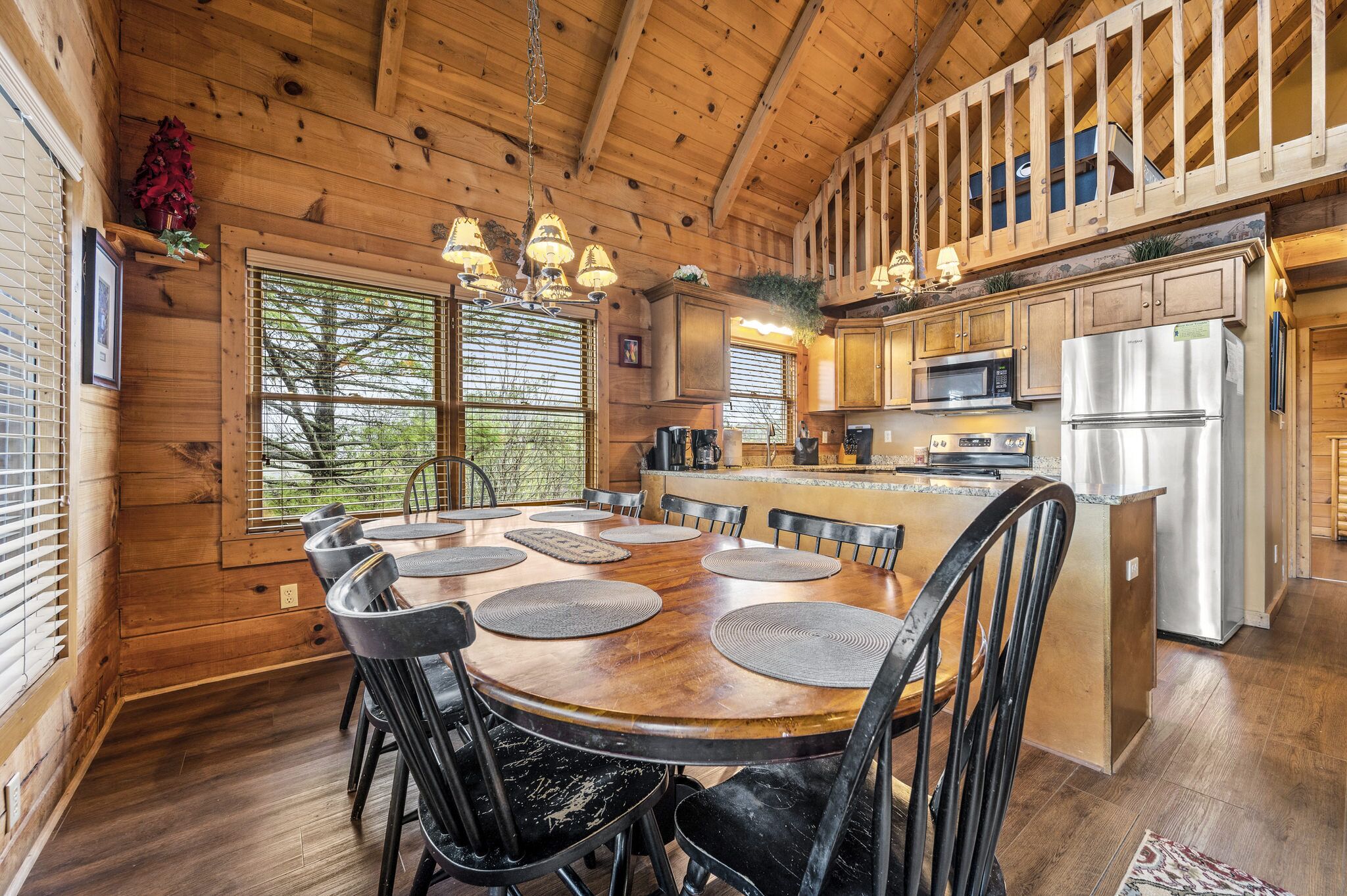 A wooden cabin interior with a dining area, kitchen, and large windows.