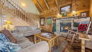 Acogedor interior de cabaña de madera con chimenea de piedra, escalera de madera y asientos cómodos.