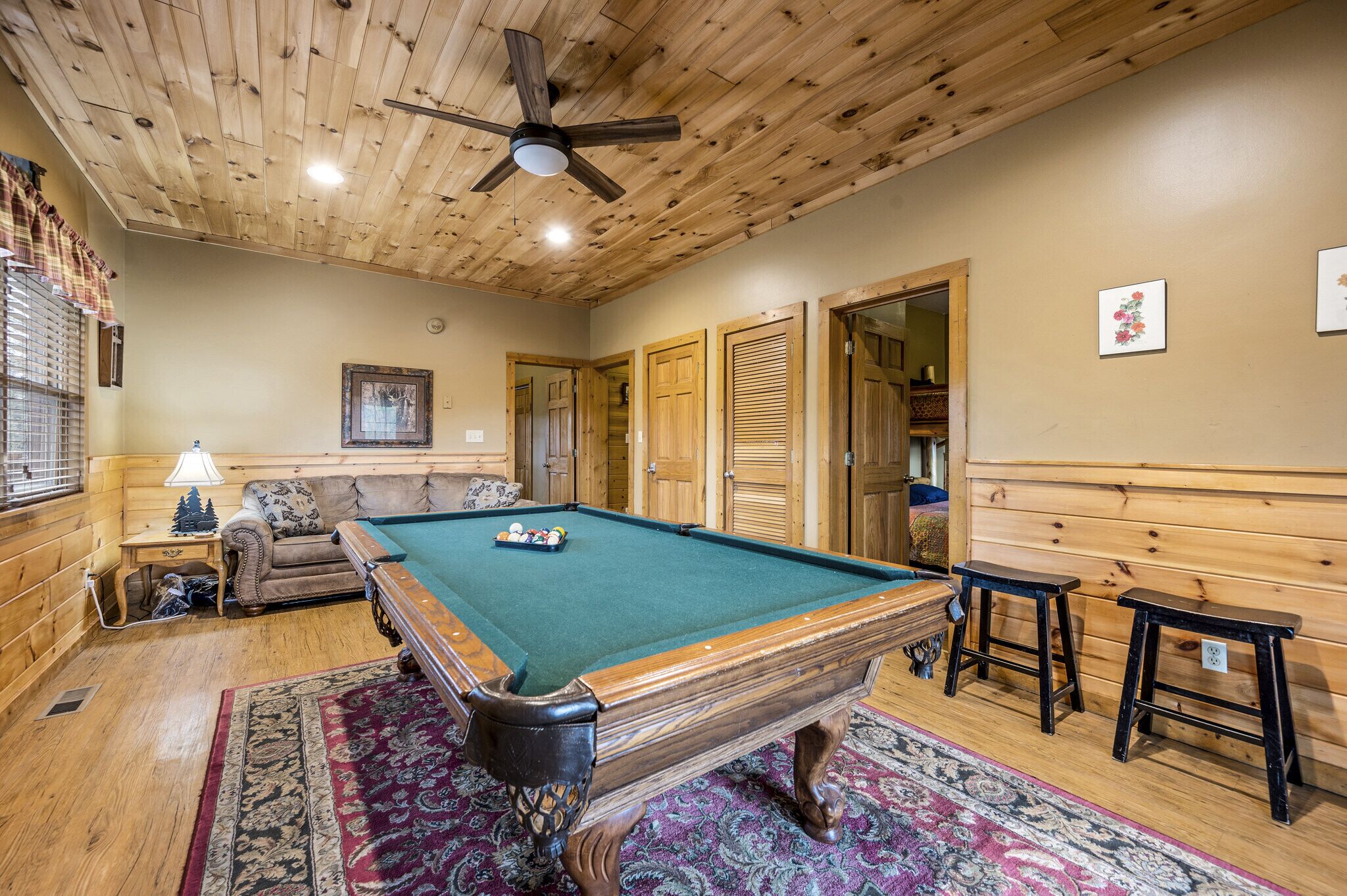 Une table de billard dans une pièce aux murs et au plafond en bois, avec un ventilateur de plafond et un tapis à motifs.