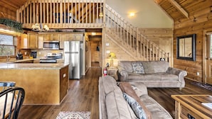 Amplia sala de estar con una escalera de madera, una cocina con electrodomésticos modernos y un rincón de estar acogedor.