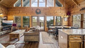 Una cabaña de madera espaciosa con un amplio comedor, una sala de estar acogedora con sofá y chimenea, y una cocina con encimera de granito.