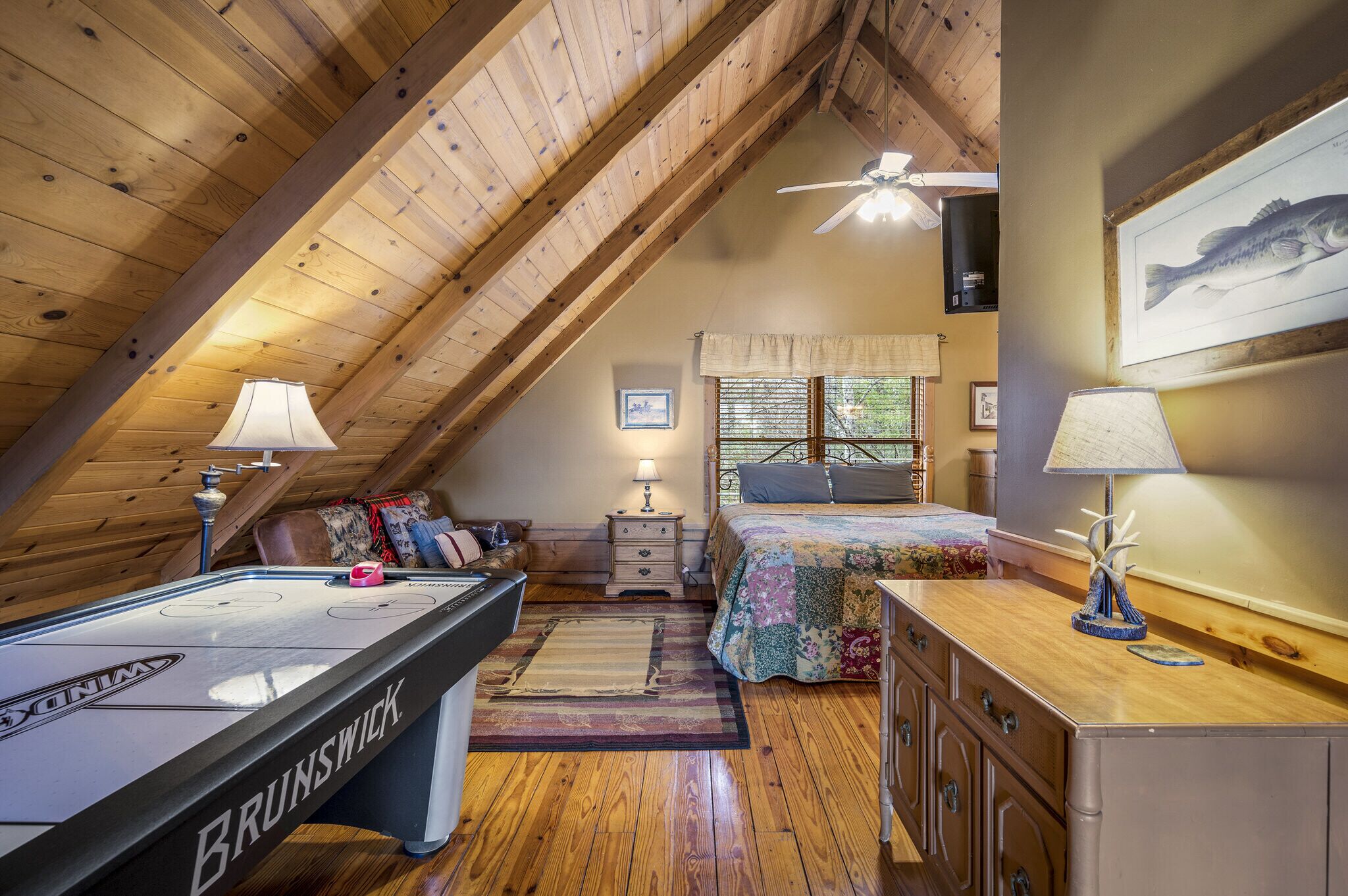 A cozy attic bedroom with a pool table, a bed with a floral bedspread, and a ceiling fan.