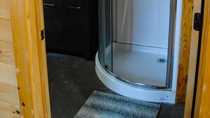 Ein Holzblock-Interieur mit einer Duschkabine aus Glas, einem Waschbecken und einer kleinen Ablagefläche.