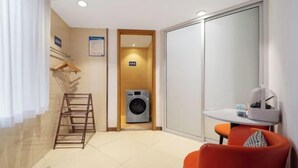 A compact hotel room with a washing machine, a small table with a chair, and a sliding door closet. - Raspberry Boutique Hotel (Lanzhou)