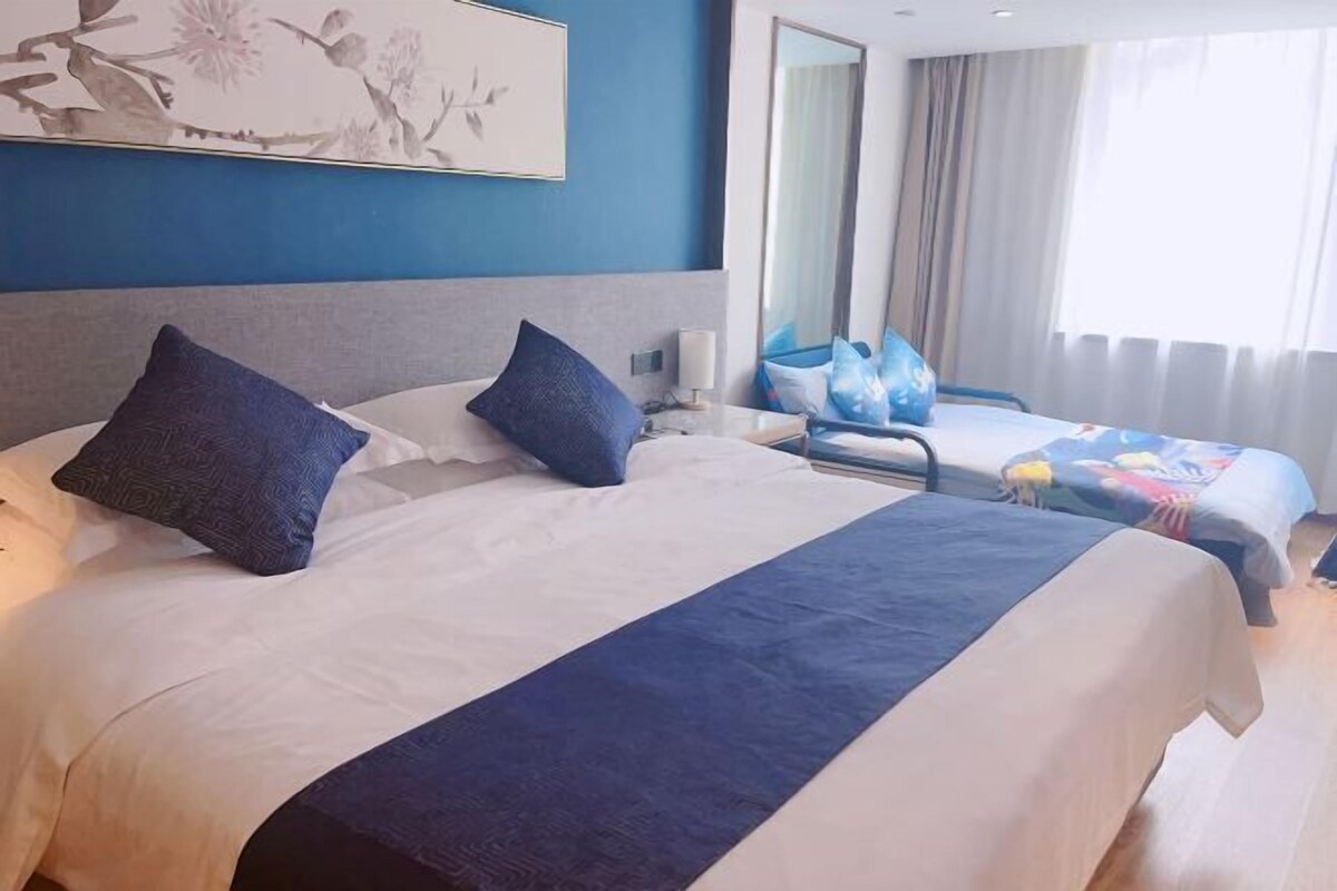 A hotel room with a large bed, two pillows, a bedside table, a lamp, and a window with curtains.