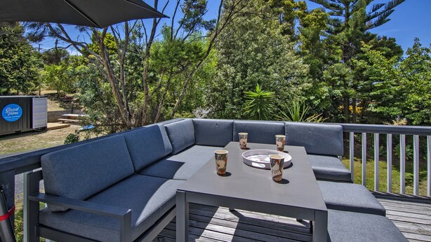 Eine Terrasse mit einem grauen Ecksofa und einem Tisch mit vier Tassen und Untertellern.