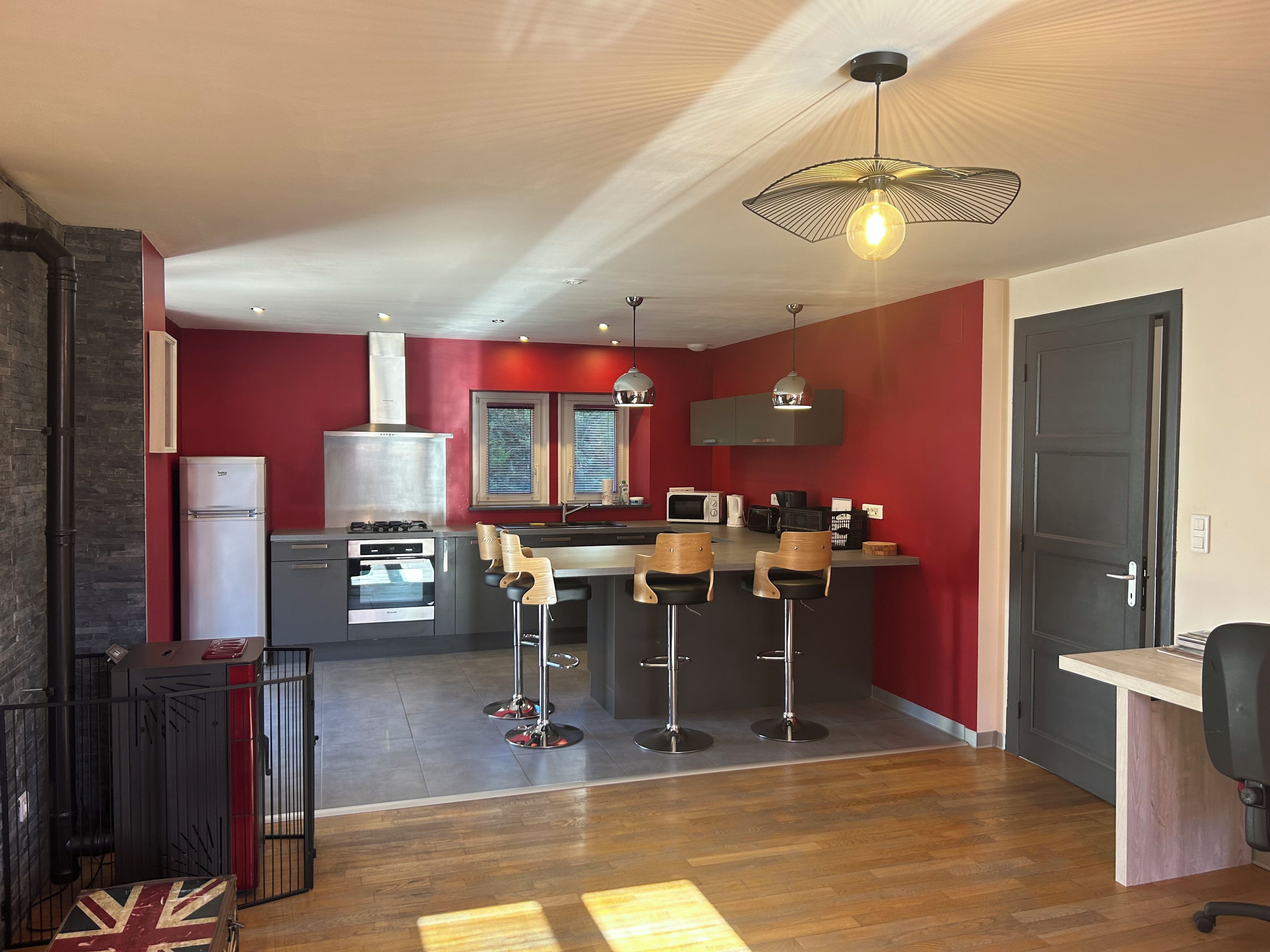 A modern kitchen with a red accent wall, a central island with bar stools, and a dining area with a wooden table and chairs.