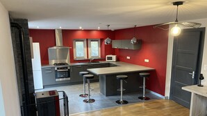 A modern kitchen with red walls, stainless steel appliances, and a bar area with stools. - City center apartment (La Bresse)