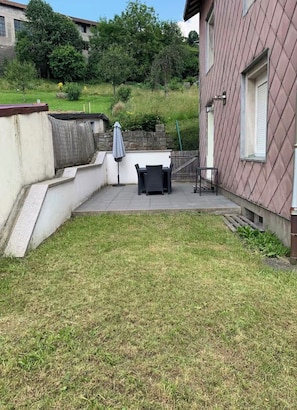 Une terrasse avec une table et des chaises, un espace abrité et une cour gazonnée.