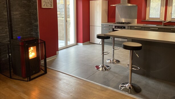 A modern kitchen with a central island, bar stools, a stove, and a large window. - City center apartment (La Bresse)