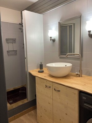 A modern bathroom with a wooden vanity, a white sink, a mirror, and a shower enclosure.