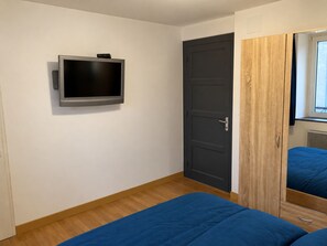 A bedroom with a single bed, a television mounted on the wall, and a wardrobe with a mirror.