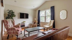 A living room with a brown leather sofa, patterned armchair, and a coffee table. A flat-screen TV is mounted on the wall, and there is a window with curtains. - The Studio at Cleveland Park 2 bedroom 2 bathroom Near Lower Broadway (Nashville)