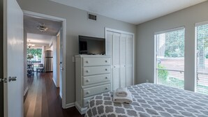 Une chambre à coucher avec un lit, une commode, un téléviseur posé dessus et une fenêtre avec des stores.