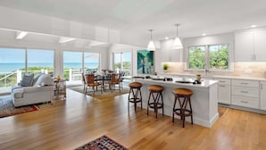 A modern kitchen with a large island, bar stools, and a view of the ocean.