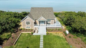 A two-story house with a large front lawn, a deck, and a view of the sea.