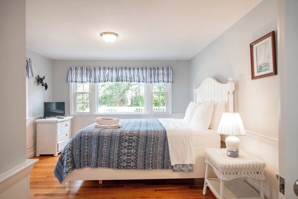 A bedroom with a bed, a bedside table with a lamp, a TV, and a window with curtains.