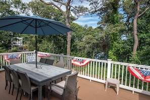 An outdoor patio with a table and chairs, a blue umbrella, and a white railing with American flags.