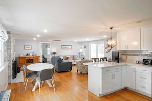A spacious living area with a dining table, sofas, and a kitchen with white cabinets and a central island.