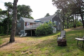 A two-story house with a covered porch, a fenced deck, and a small outdoor seating area with chairs and a table.