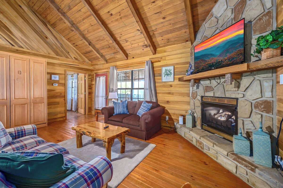 L’intérieur chaleureux d’un chalet avec une cheminée en pierre, un plafond en bois et des meubles à motifs écossais.