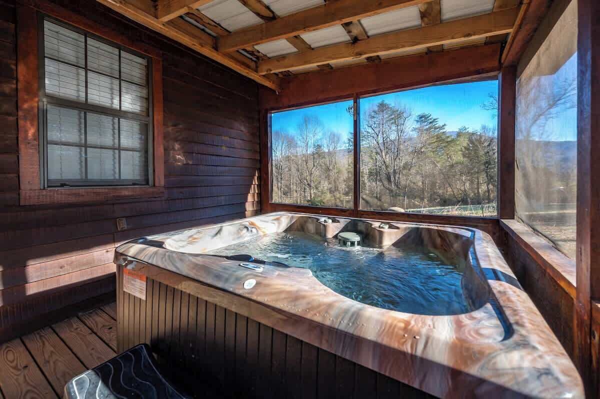 Een houten hut met een whirlpool en een groot raam met uitzicht op een bos.