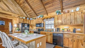 L’intérieur d’un chalet en bois comprend une cuisine équipée d’un réfrigérateur, d’un four à micro-ondes, d’une cuisinière, d’un évier et d’armoires en bois.