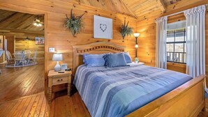 Une chambre dans une cabane en bois, avec un lit, des tables de chevet et une fenêtre avec des rideaux.