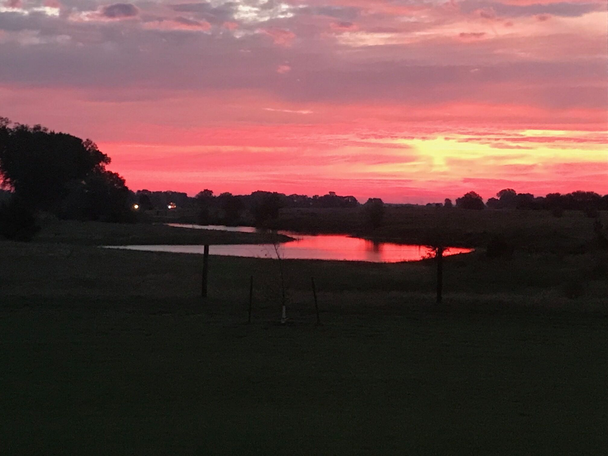 Een ondergaande zon boven een wateroppervlak met een hek op de voorgrond.