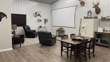 A room with a dining table, chairs, a sofa, a TV, and mounted animal heads on the wall.