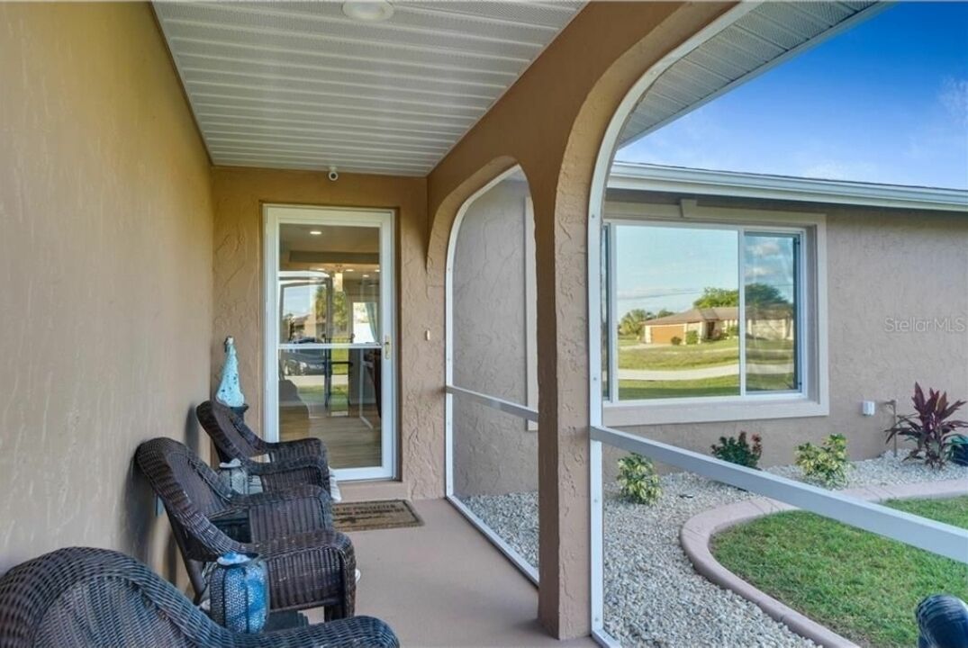 A covered outdoor area with wicker chairs, a glass door leading inside, and a view of a residential area.