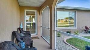 A covered outdoor area with wicker chairs, a glass door leading inside, and a view of a residential area. - Casa Florida, Pet-friendly, Child-friendly  (Port Charlotte)