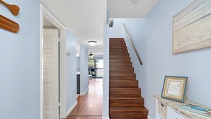 Un couloir avec un escalier en bois, une porte donnant sur une pièce et un panneau d’accueil encadré posé sur une console.