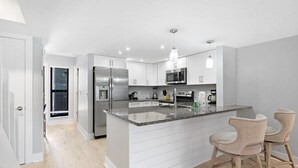 Een moderne keuken met roestvrijstalen apparatuur, een granieten aanrechtblad en een kleine eethoek met twee stoelen.