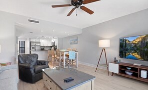 Una sala de estar moderna con un sofá de cuero, una mesa de centro de vidrio, un televisor y un comedor con una mesa y sillas de madera.