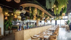 A restaurant with a long counter, wooden chairs, and hanging plants. - Umhlanga Arch - Ocean Views, Queen Size Bed, Free Wifi (Umhlanga)