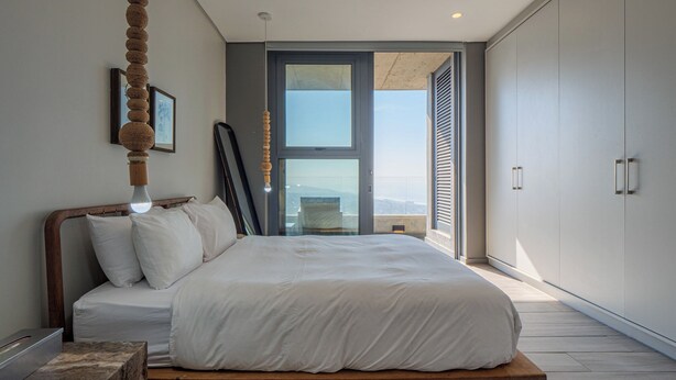 A modern bedroom with a large bed, a view of the city through a glass door, and a hanging light fixture. - Umhlanga Arch - Ocean Views, Queen Size Bed, Free Wifi (Umhlanga)