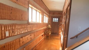 Un pasillo con paredes y suelos de madera, una puerta al fondo y una lámpara a la derecha.