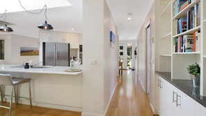 A modern kitchen with a central island, stainless steel appliances, and a bookshelf filled with books. - Brighter Times - A private Haven, a place of calm. (BRIGHT)