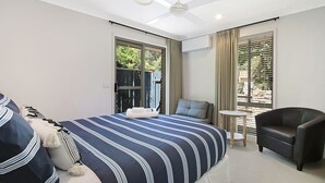 A hotel room with a large bed, a chair, a small table, and a window with curtains. - Brighter Times - A private Haven, a place of calm. (BRIGHT)