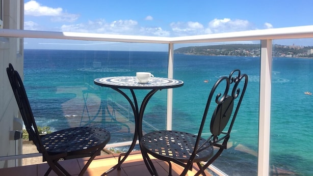 A balcony with two chairs and a table, overlooking a clear blue sea with a distant shoreline. - Manly Waterfront Beach Stay (Queenscliff)