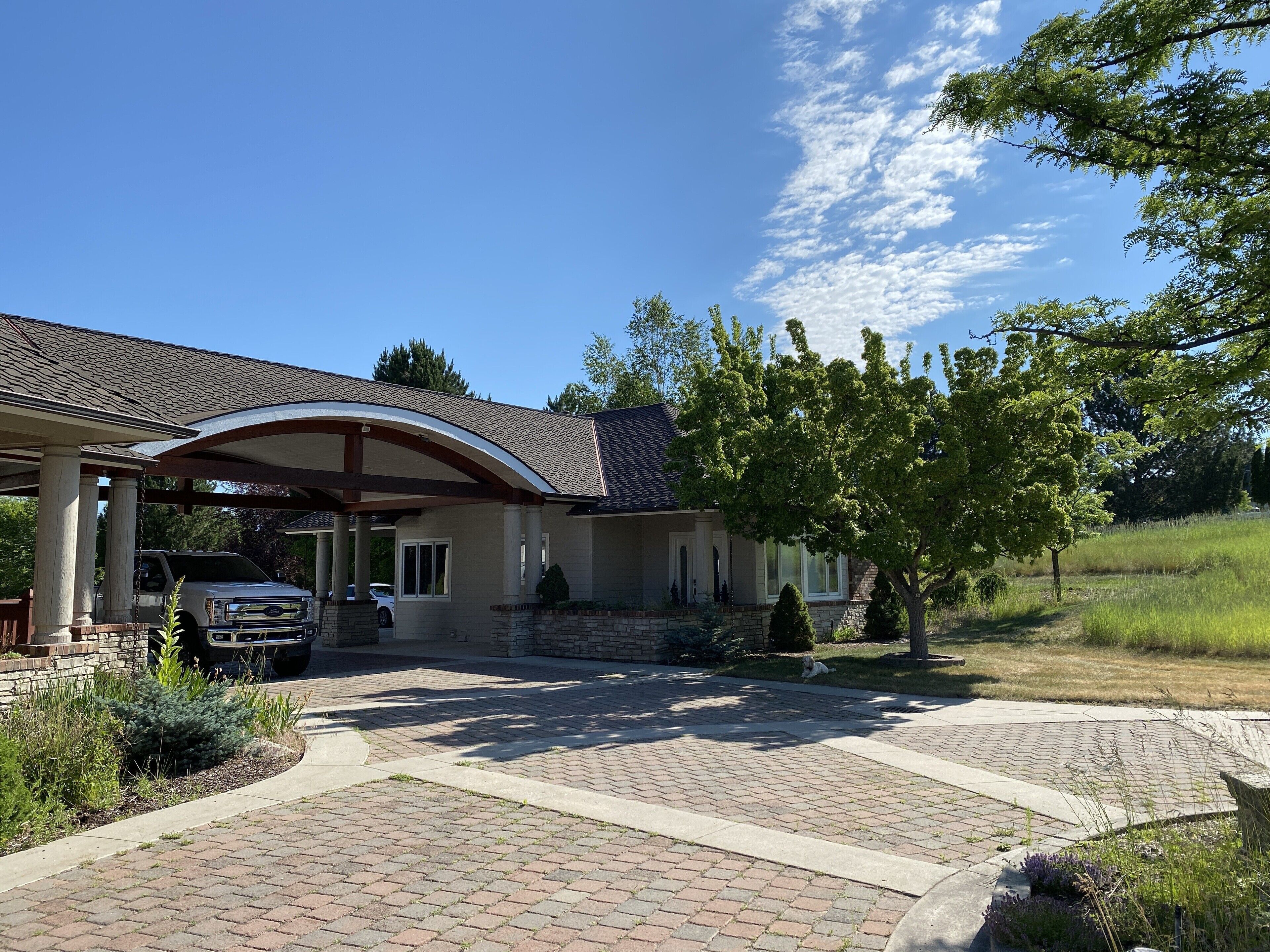 A house with a covered porch, a brick driveway, and a lawn.