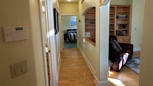 A hallway with wooden flooring, a ceiling light, a thermostat, and a bookshelf.
