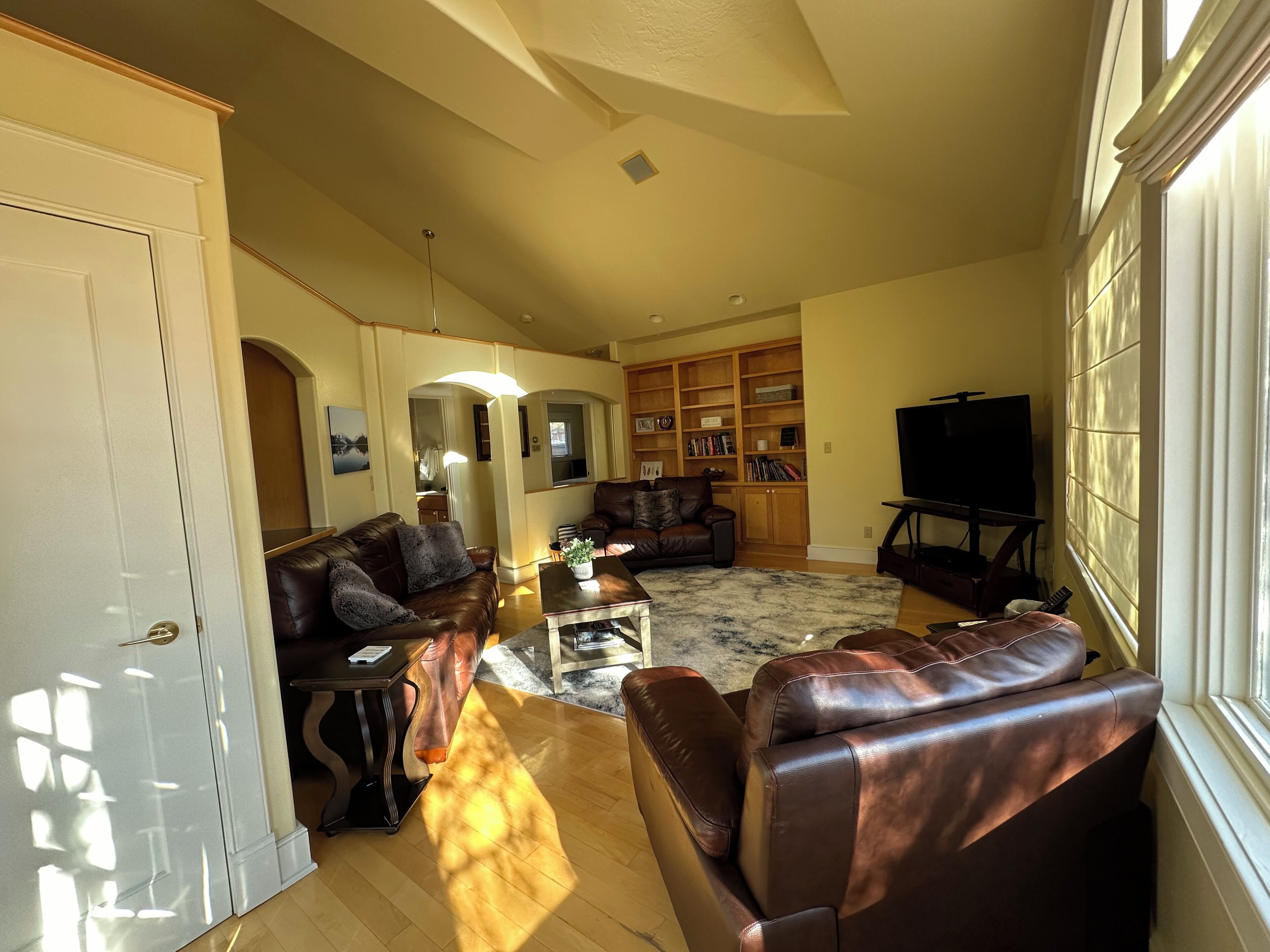 A spacious living room with leather sofas, a coffee table, and a bookshelf.
