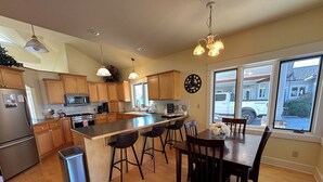 A modern kitchen with wooden cabinets, a central island with bar stools, a refrigerator, and a large window providing a view of the outside.